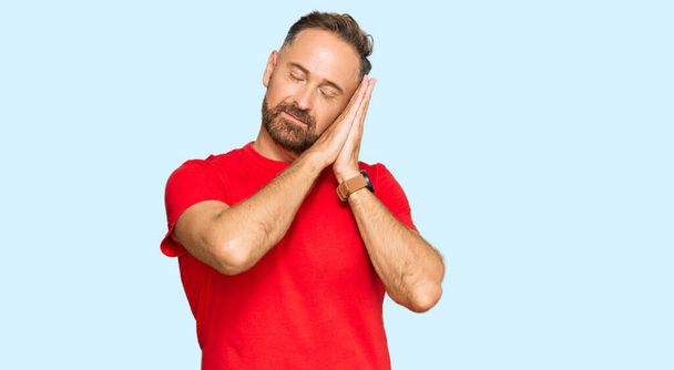 Handsome middle age man wearing casual red tshirt sleeping tired dreaming and posing with hands together while smiling with closed eyes.  - Photo, image