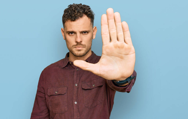 Young hispanic man wearing casual clothes doing stop sing with palm of the hand. warning expression with negative and serious gesture on the face.  - Photo, Image