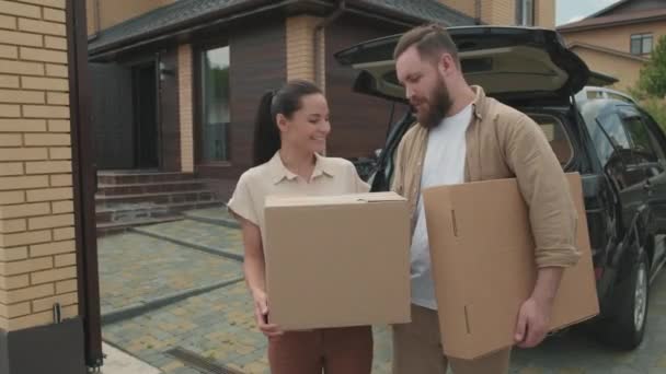  Porträt einer glücklichen jungen Frau und eines bärtigen Mannes, die Pappkartons halten und vor ihrem neuen Haus für die Kamera posieren - Filmmaterial, Video