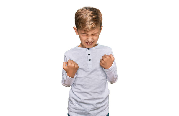 Petit garçon caucasien portant des vêtements décontractés très heureux et excité faisant geste gagnant avec les bras levés, souriant et criant pour le succès. concept de célébration.  - Photo, image