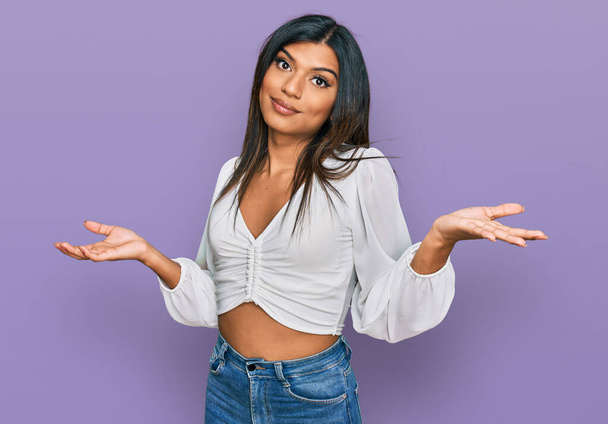 Young latin transsexual transgender woman wearing casual clothes clueless and confused expression with arms and hands raised. doubt concept.  - Foto, Imagen