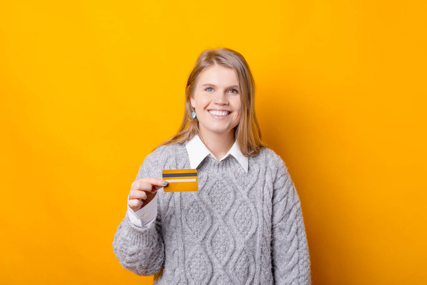 Радісна молода жінка тримає кредитну картку і дивиться на камеру посміхається
 - Фото, зображення