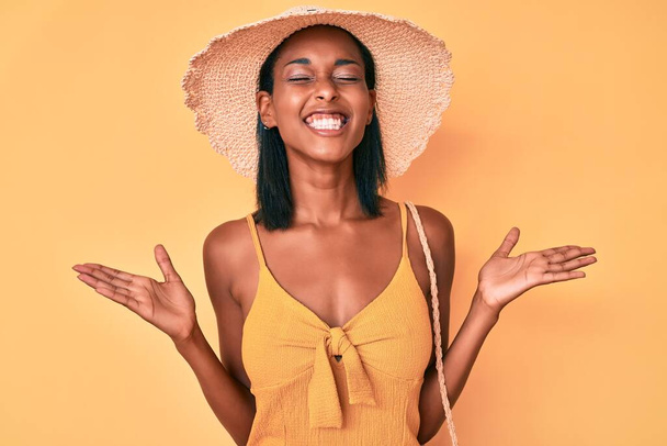 夏の帽子をかぶっている若いアフリカ系アメリカ人女性は、腕を上げて興奮して叫んで目を閉じて成功のために狂気と狂気を祝います。勝者のコンセプト  - 写真・画像