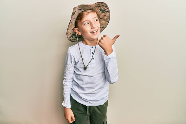 小さなcaucasian男の子子供身に着けていますエクスプローラ帽子指して親指へザ側笑顔幸せとともにオープン口  - 写真・画像
