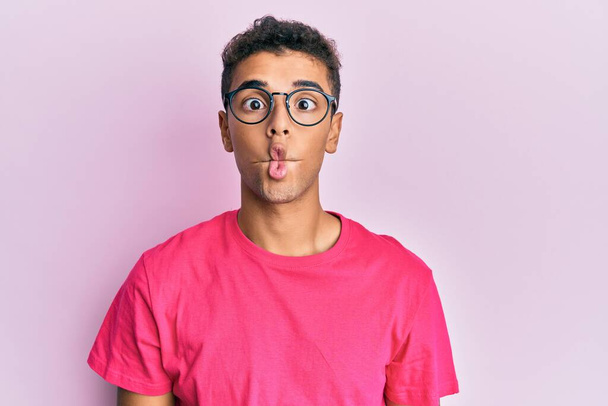 Young handsome african american man wearing glasses over pink background making fish face with lips, crazy and comical gesture. funny expression.  - Foto, immagini