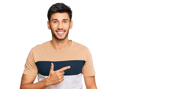 Young handsome man wearing casual clothes cheerful with a smile on face pointing with hand and finger up to the side with happy and natural expression  - Photo, Image