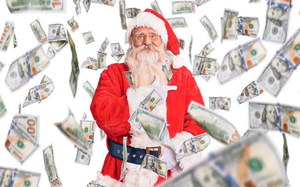 Старий старший чоловік з сірим волоссям і довгою бородою в традиційному костюмі Санта-Клауса веселий з посмішкою на обличчі вказуючи рукою і пальцем на бік з щасливим і природним виразом
 - Фото, зображення