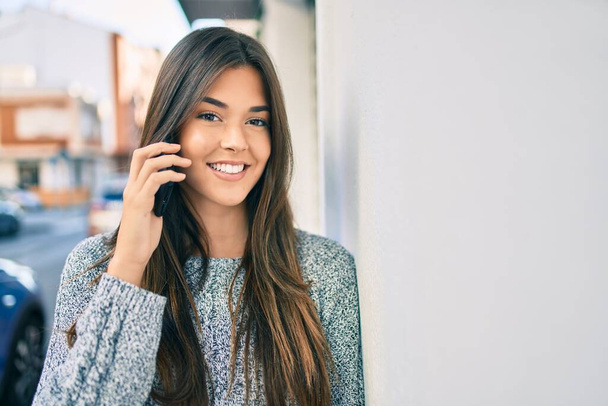 Joven chica hispana hermosa sonriendo feliz hablando en el teléfono inteligente en la ciudad. - Foto, imagen