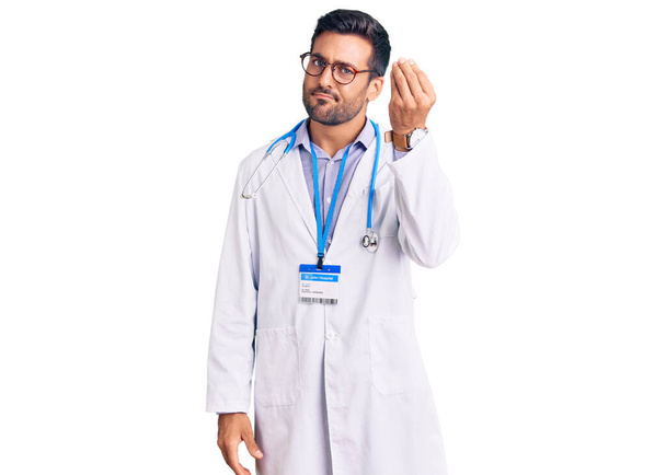 Young hispanic man wearing doctor uniform and stethoscope doing italian gesture with hand and fingers confident expression  - Фото, зображення