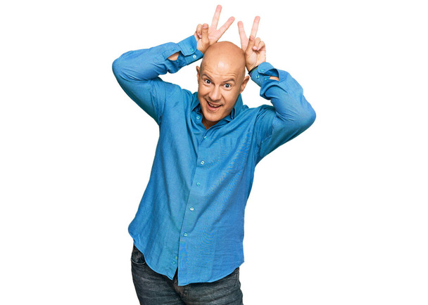 Középkorú kopasz férfi alkalmi ruhát visel pózol vicces és őrült ujjakkal a fején, mint nyuszifül, mosolygós vidám  - Fotó, kép