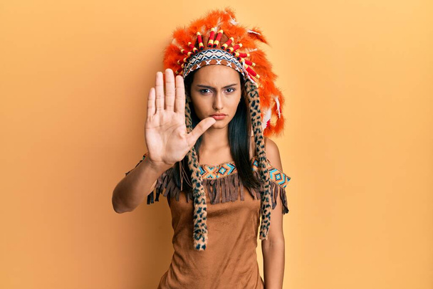 Mladá brunetka v indiánském kostýmu přestala zpívat dlaní. varovný výraz s negativním a vážným gestem na tváři.  - Fotografie, Obrázek