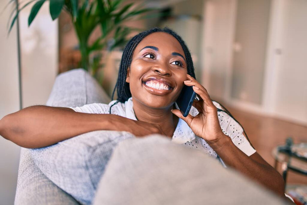 Mladý africký americký žena usměvavý šťastný sezení pomocí smartphone doma - Fotografie, Obrázek