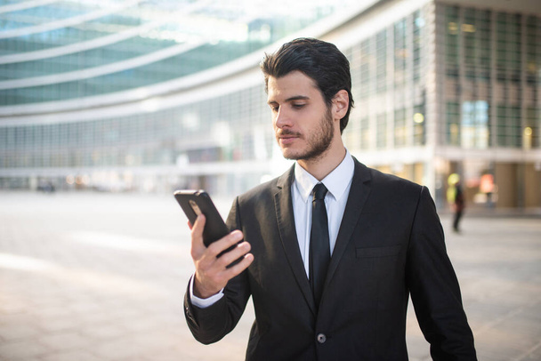 Handsome businessman reading a message on his smartphone outdoor in a modern city setting - Fotoğraf, Görsel
