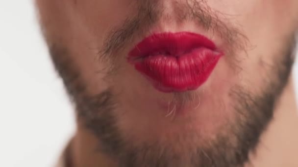 Vista de cerca de la boca masculina usar maquillaje lápiz labial rojo en los labios. Un hombre metrosexual o gay con barba negra, bigote come deliciosos dulces de azúcar aislados sobre fondo blanco. Concepto de la dulce vida - Metraje, vídeo