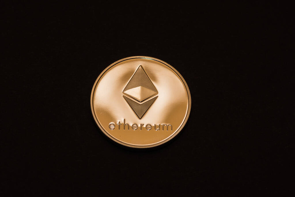 waardevol glanzend goud ether munt uit cryptogeld midden op zwarte achtergrond - Foto, afbeelding