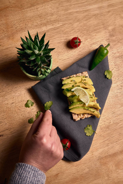 healthy vegan breakfast. avocado toast with lime and coriander on top of a dark napkin on a wooden background - Fotografie, Obrázek