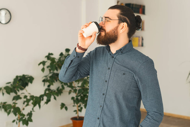 A young bearded man is drinking a hot drink in office - 写真・画像