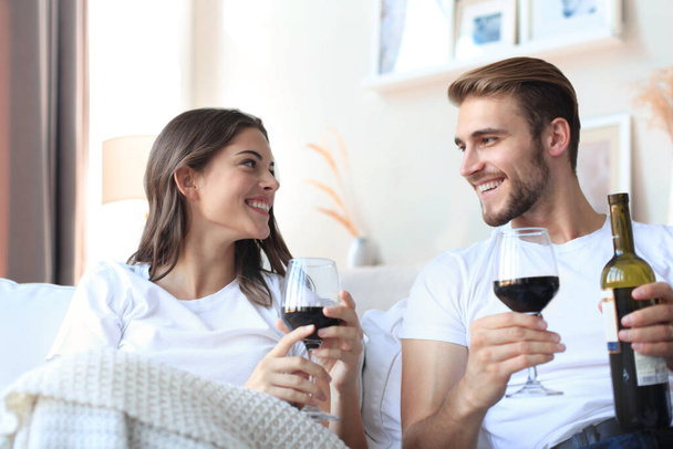 Young loving couple drinking a glass of red wine in their living room - 写真・画像