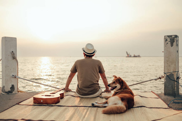 A man wear straw hat and hug with a dog relax near the sea sunset - Foto, Bild