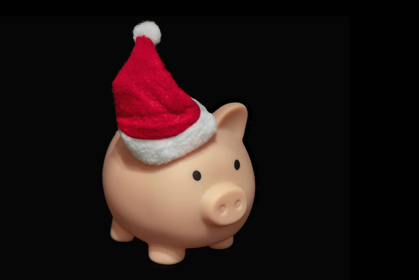 Pink piggy bank in Santa hat on black background. The concept of savings. Free space - Photo, Image
