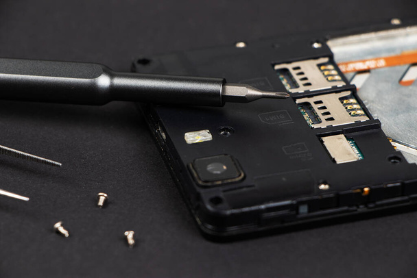 Broken mobile phone and repair tools on dark background, flat lay - Фото, изображение