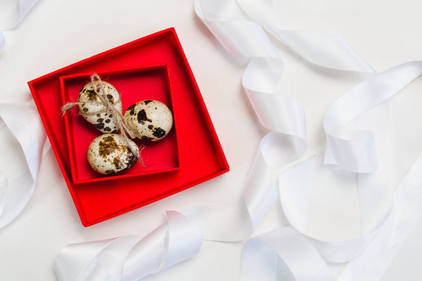 Three quail eggs in a red box on a background of white ribbons - Foto, Bild