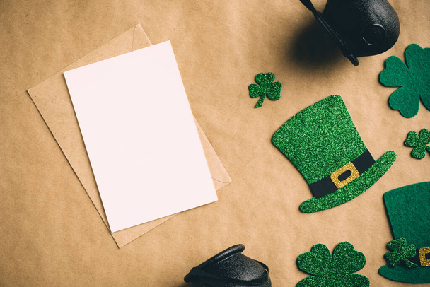 Happy St Patrick's Day concept. Vintage flat lay composition with blank greeting card mockup, leprechaun hats, clover shamrock leaves, pots of gold on kraft paper background. - Fotografie, Obrázek