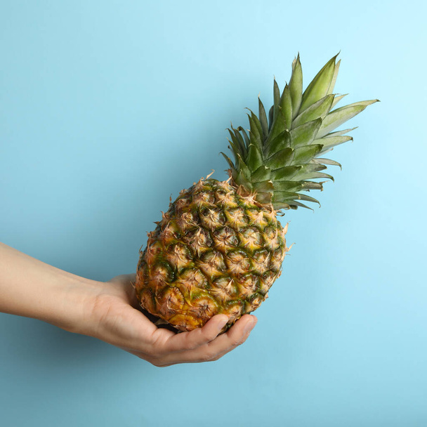 Female hand hold ripe pineapple on blue background - Zdjęcie, obraz