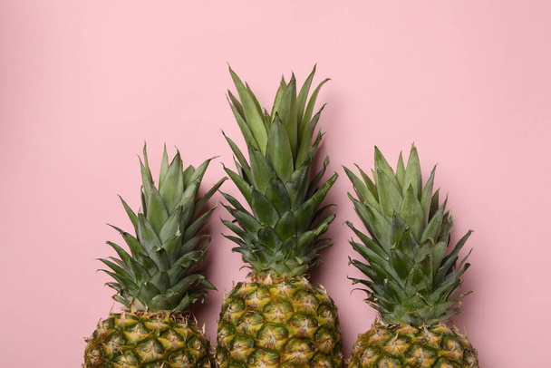 Three tasty ripe pineapples on pink background - Фото, зображення