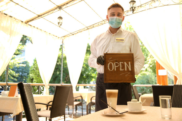 Waiter holding OPEN sign in restaurant. Catering during coronavirus quarantine - Photo, image