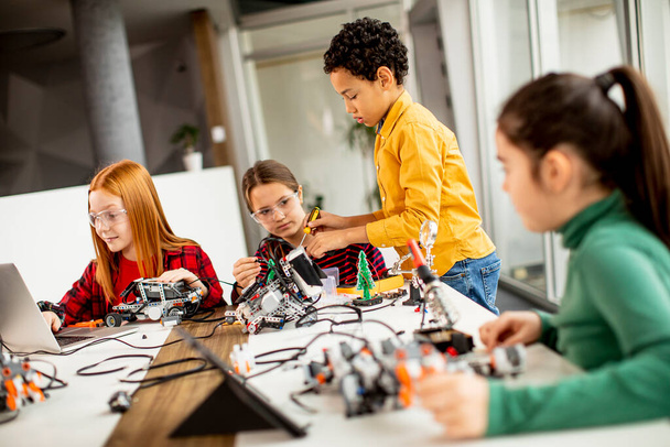 Группа счастливых детей программирует электрические игрушки и роботов в классе робототехники - Фото, изображение
