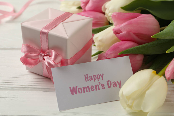 Text Happy Women 's Day, tulipány a dárková krabička na bílém dřevěném pozadí, zblízka - Fotografie, Obrázek
