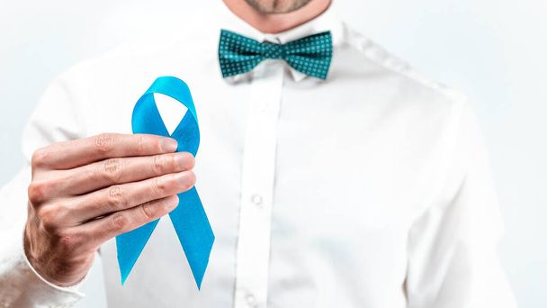 Μπλε κορδέλα για καρκίνο. Ευαισθητοποίηση προστάτη της υγείας το Νοέμβριο. Hipster άνδρες σε φωτεινό πουκάμισο, κυανό παπιγιόν με μπλε κορδέλα στα χέρια σε λευκό φόντο. Σύμβολο της ογκολογίας επηρεάζονται άνθρωπος. Αντιγραφή χώρου - Φωτογραφία, εικόνα