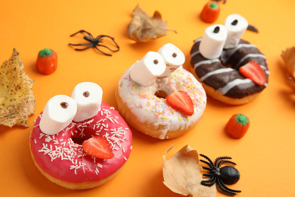 Delicious donuts decorated as monsters on orange background. Halloween treat - Zdjęcie, obraz