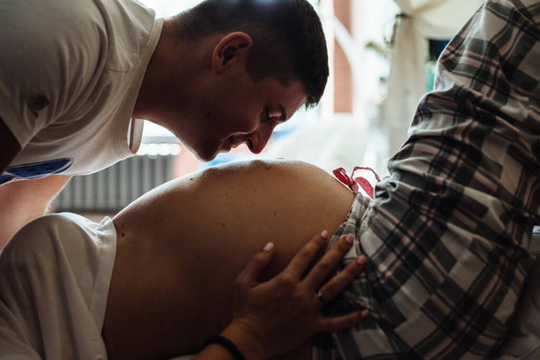 Imagen de feliz futuro papá besando vientre de su esposa embarazada caucásica alegre acostado en la cama en casa, de cerca. Ruido de película - Foto, Imagen
