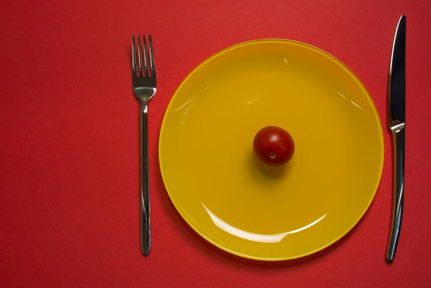 Dieta concetto piatto vista dall'alto. Pomodoro ciliegia su piatto giallo vuoto con coltello e forchetta su fondo rosso. Perdita di peso dieta concetto - Foto, immagini