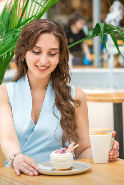Piękna młoda biała kobieta siedząca przy stole z ciastkami i filiżanką kawy w kawiarni na świeżym powietrzu - Zdjęcie, obraz