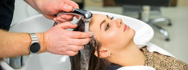 Un peluquero masculino comienza a lavar el cabello de una joven en un lavabo en una peluquería - Foto, imagen