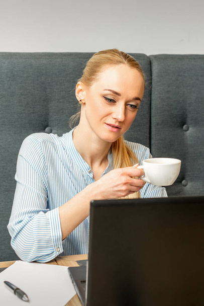 Portrait of a young businesswoman using laptop sitting at the table with a cup of coffee in a cafe - Photo, image
