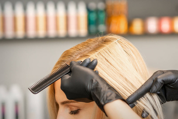Peinador peina el cabello femenino antes de teñirse en un salón de belleza - Foto, imagen