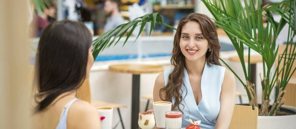 Zwei schöne junge kaukasische Frauen trinken Kaffee sitzend am Tisch im Café im Freien - Foto, Bild