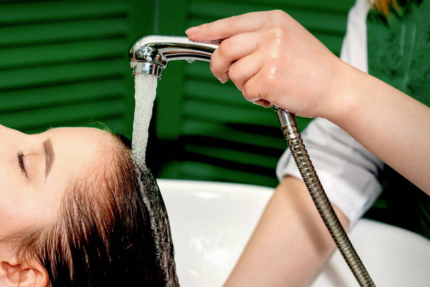 Вид збоку фото молодої білої жінки, яка приймає прання волосся в перукарні
 - Фото, зображення