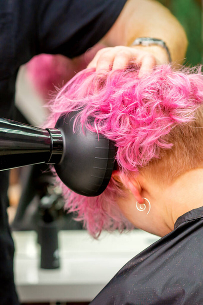 Close up de cabeleireiro secagem cabelo curto rosa ou vermelho com um secador de cabelo em um salão de beleza - Foto, Imagem