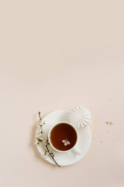 Posa piatta di tazza di tè in piedi con fiori di mela e marshmellow su sfondo beige con spazio copia - Foto, immagini