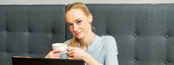 Πορτρέτο μιας νεαρής επιχειρηματία που χρησιμοποιεί φορητό υπολογιστή κάθεται στο τραπέζι με ένα φλιτζάνι καφέ σε ένα καφέ - Φωτογραφία, εικόνα