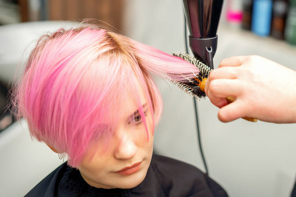 Fryzjer suszy różowe włosy młodej kobiety w salonie piękności - Zdjęcie, obraz