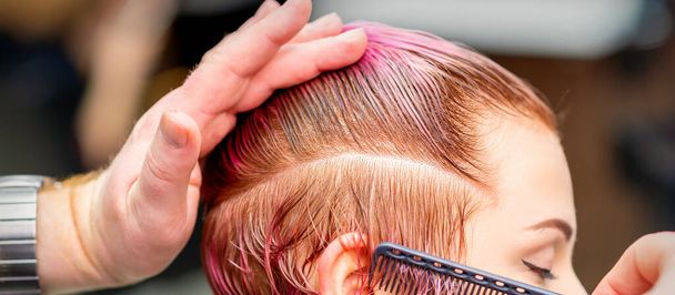 Cabeleireiro masculino pentear o cabelo fazendo penteado rosa curto para uma jovem mulher branca em um salão de beleza - Foto, Imagem