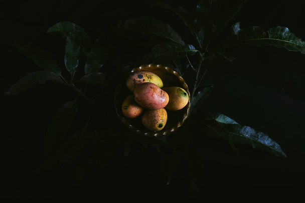 A top viewcloseup view of ripe mangoes inside of a brown ceramic bowl next to leaves - Foto, afbeelding