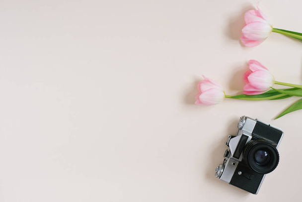 Photocamera retro i różowe tulipany na beżowym ciemnym tle. Szablon do reklamy lub wizualizacji bloga z miejsca kopiowania, miejsce tekstowe. Widok góry. Koncepcja wiosny - Zdjęcie, obraz