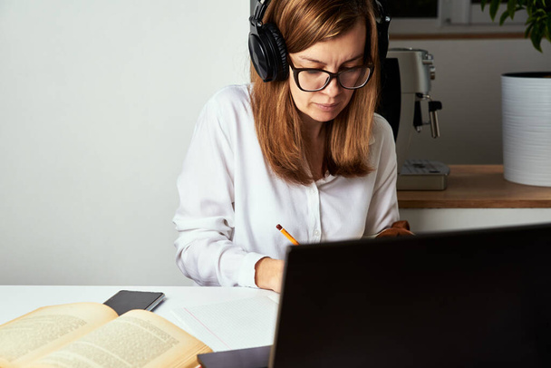 Uzaktan kumanda. Çevrimiçi kurs, uzaktan eğitim ve e-öğrenme konsepti. Kulaklıklı kadın dizüstü bilgisayardaki ses kursunu dinliyor. - Fotoğraf, Görsel